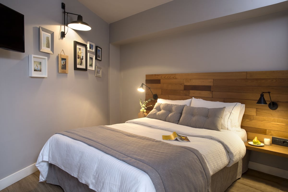 A neatly made bed with a wooden headboard, a bedside table with a lamp, and framed pictures on the wall.