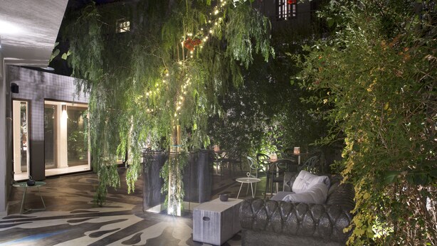 Un jardín interior con asientos, piso estampado y luces colgantes.