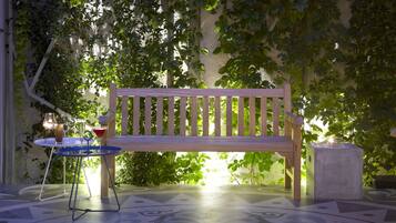 A wooden bench with a table and drinks in a shaded outdoor area with patterned flooring.