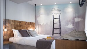 Un dormitorio con cabecera de madera, cama con almohadas, mesita de noche con jugo de naranja y un mural con una escalera y nubes.