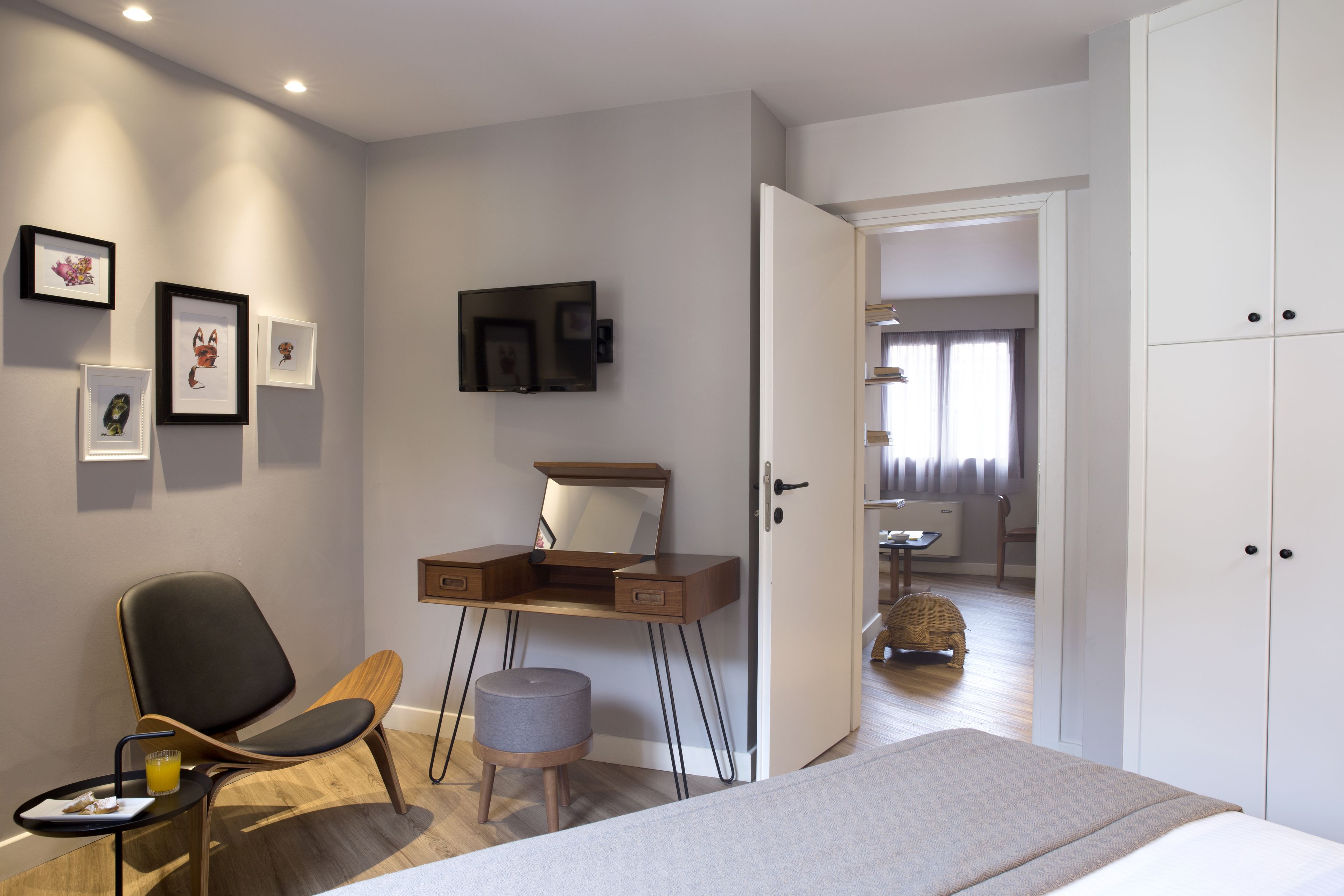 A modern bedroom with a bed, a desk with a chair, a small stool, and a wardrobe.