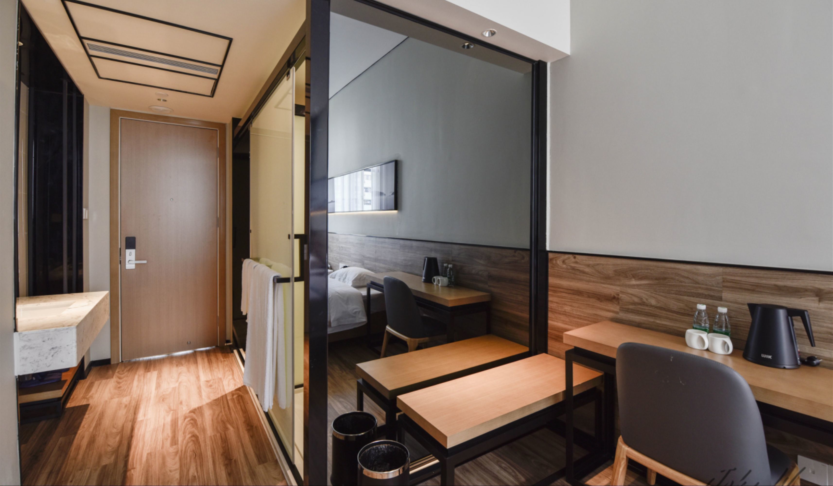 Une chambre d’hôtel moderne avec un plancher en bois, un bureau, une chaise, un lit et un grand miroir.