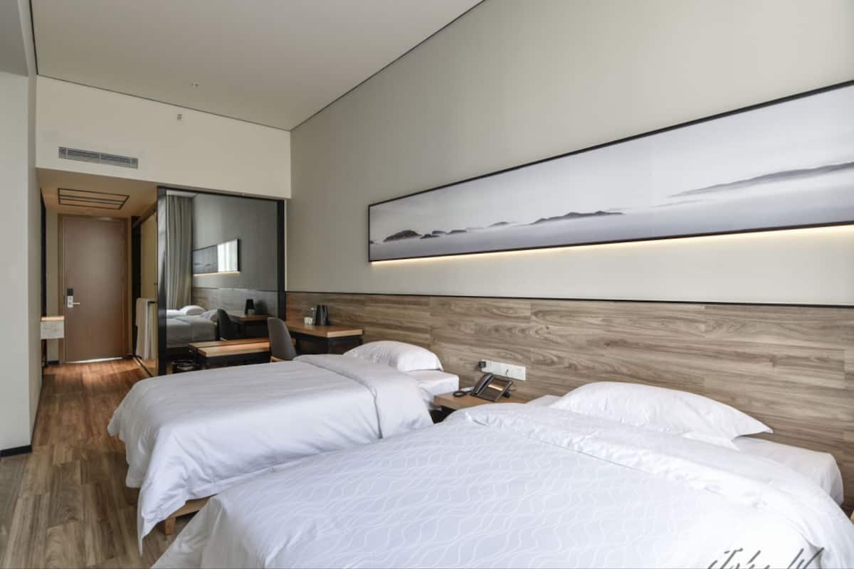 A hotel room with two beds, a desk, a chair, a mirror, and a painting on the wall.
