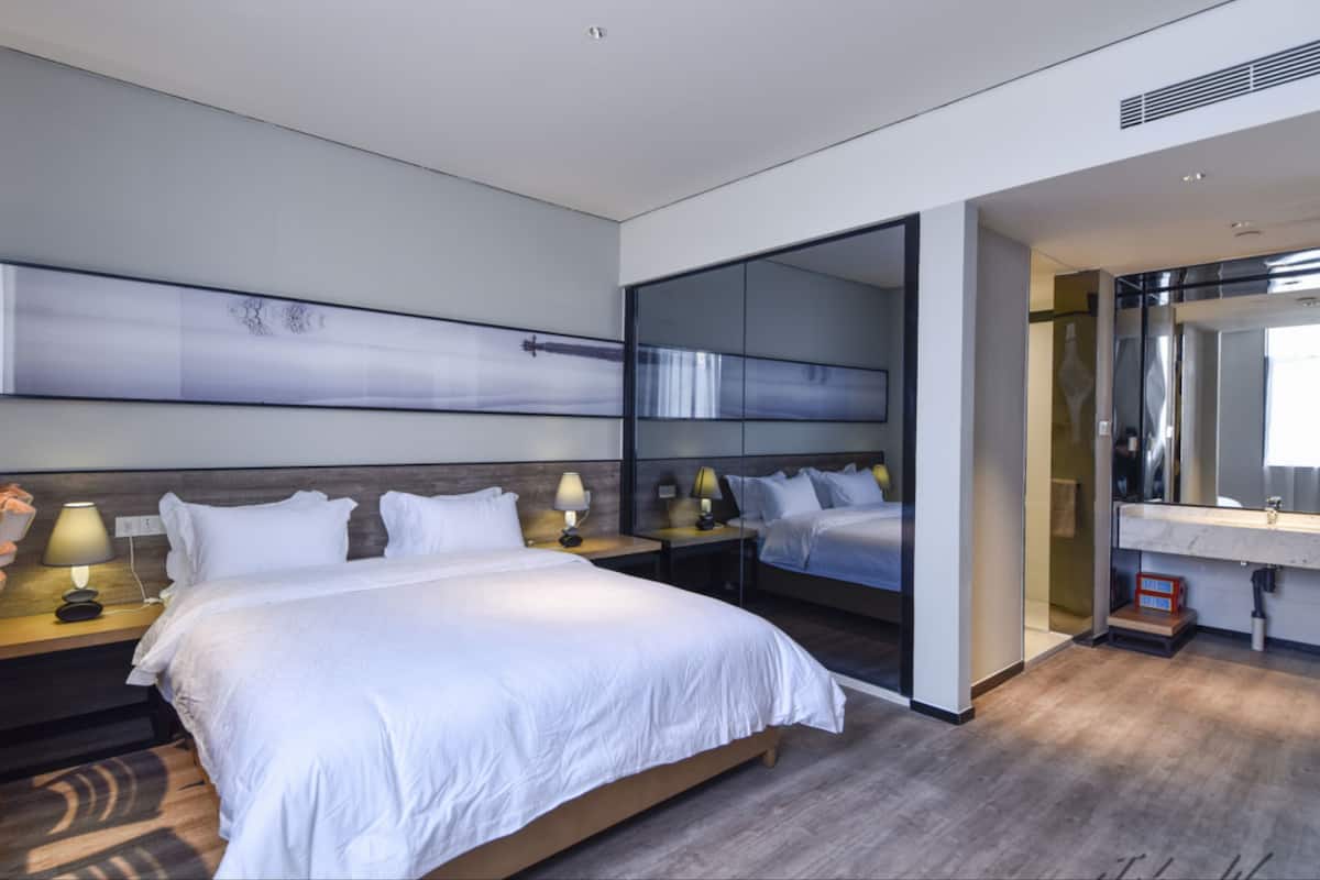 A modern hotel room with a large bed, bedside tables with lamps, a large mirror, and a view of the bathroom.