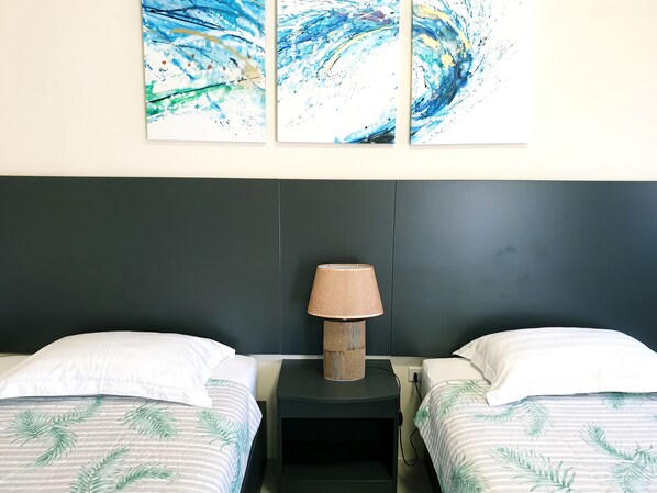 A hotel room with two beds, a nightstand with a lamp, and abstract wall art. - Clear Water Hotel (Saipan)