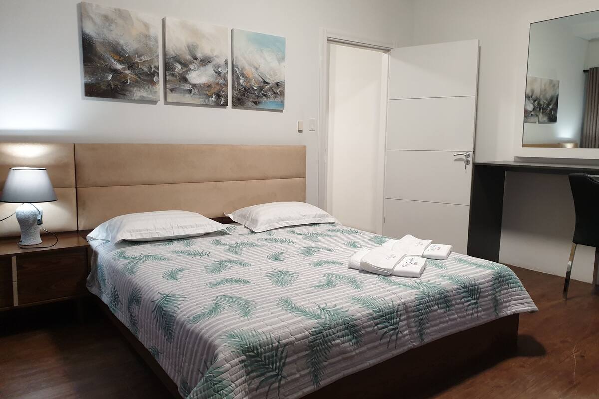 A neatly arranged bedroom with a bed, a nightstand with a lamp, a desk, and a chair.
