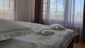 Ein Hotelzimmer mit Bett, Fenster mit Vorhängen und Blick auf den Strand.