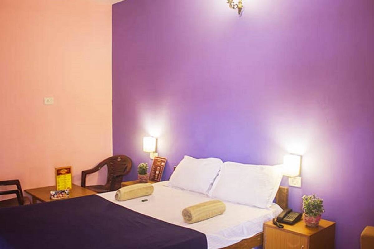 A hotel room with a bed, two bedside tables, a chair, a small table, and a lamp.