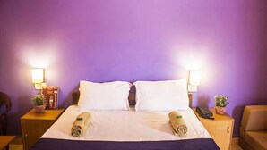 A hotel room with a bed, two nightstands, a lamp, a phone, and a small plant. - Jesus Holiday Home Resort (Candolim)