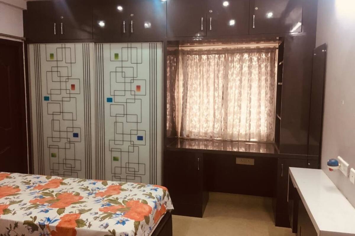 Ein Schlafzimmer mit einem Bett, einem Schreibtisch, einem Schrank mit geometrischem Muster und einem Fenster mit Vorhängen.