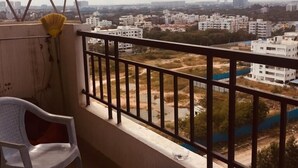 Ein Balkon mit Blick auf eine Stadtlandschaft, ein Stuhl und ein blauer Eimer.