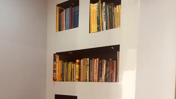 Une pièce avec un mur blanc orné de plusieurs étagères remplies d’une grande variété de livres. On y trouve également un meuble noir à deux portes, situé en bas du mur.