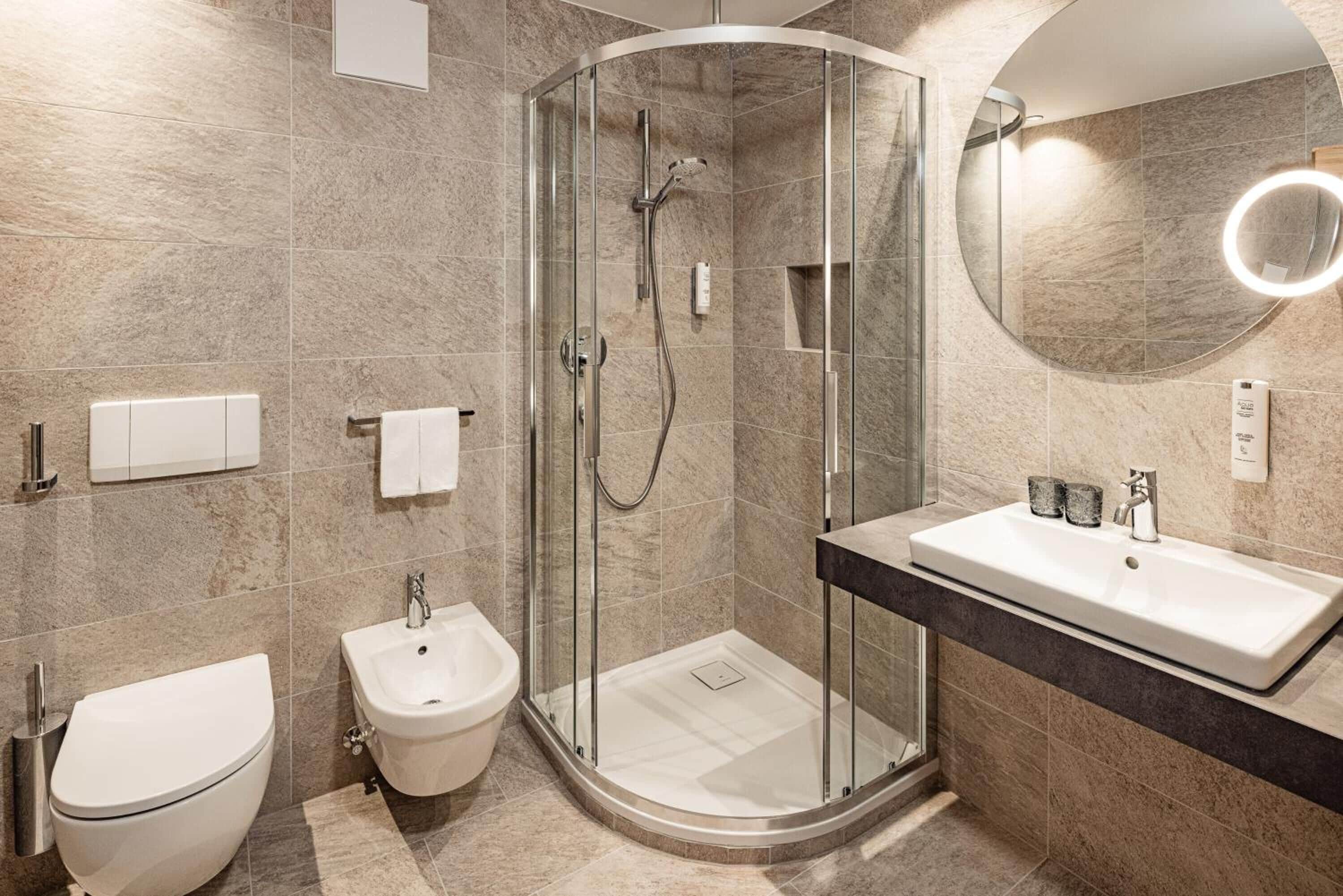 Un baño moderno con ducha de vidrio, un bidé, un inodoro y un tocador con espejo.