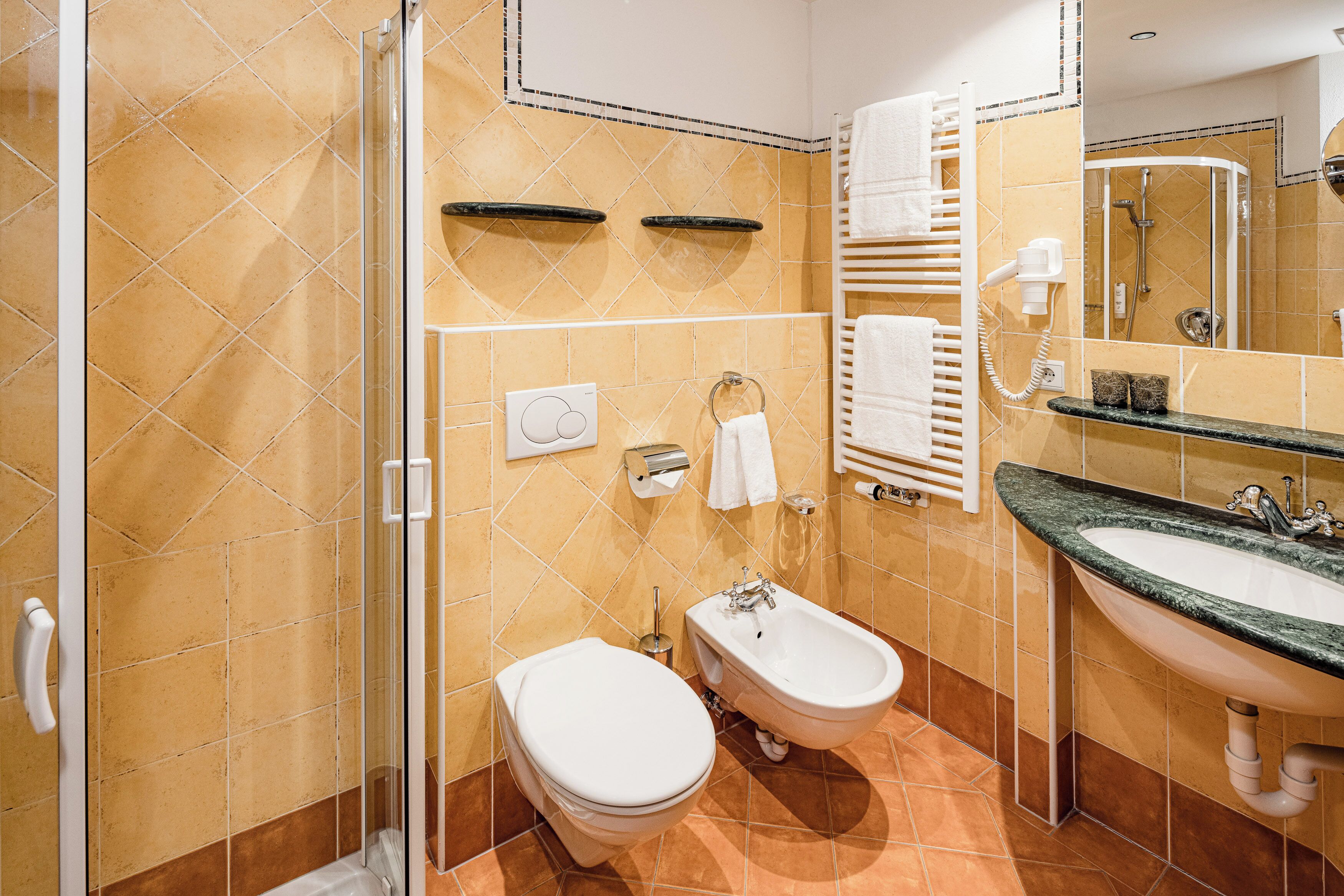 A bathroom with a shower, toilet, bidet, and sink.