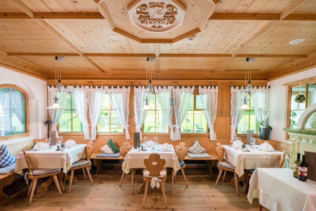 A wooden interior with multiple tables and chairs, large windows with curtains, and a decorative ceiling.