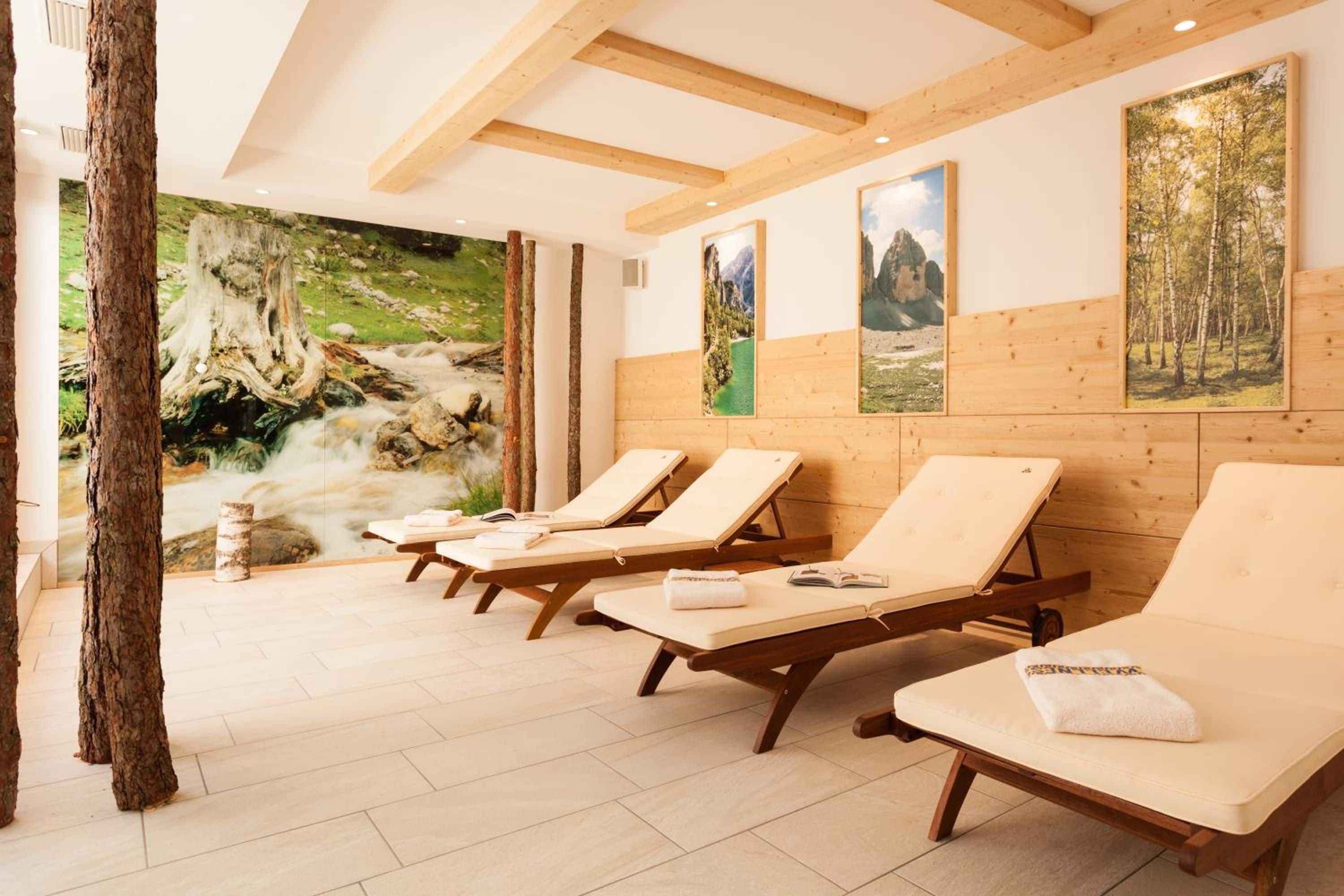 Une salle de spa avec des poutres en bois, une fresque représentant une scène de forêt et quatre fauteuils confortables avec des serviettes.