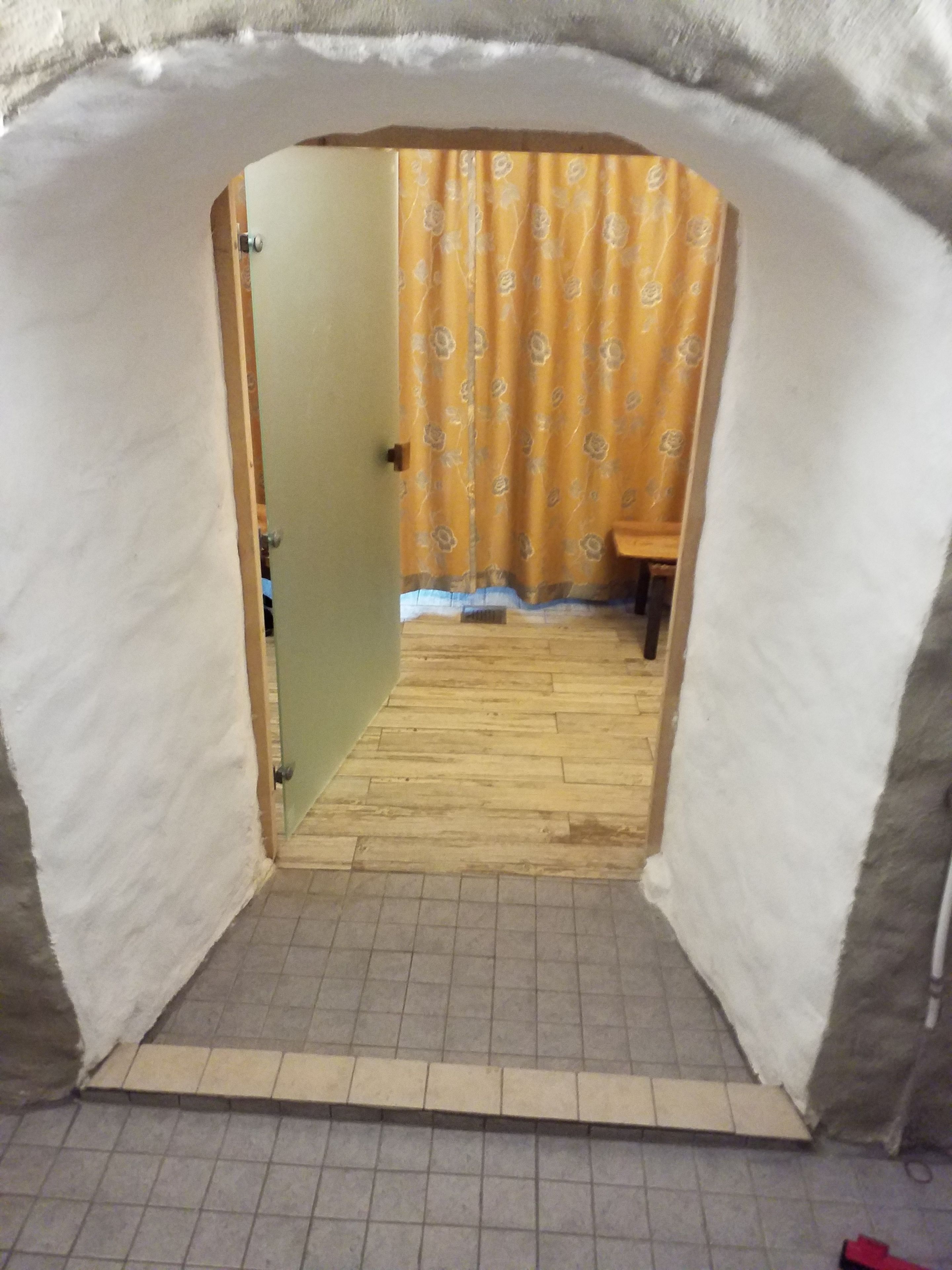 A room with a wooden floor, a door leading to another room, and a yellow curtain with a floral pattern.