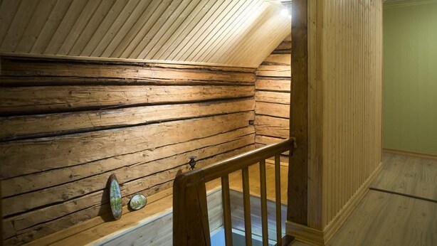 Una escalera de madera conduce a un dormitorio tipo altillo con techo inclinado y un ventanal pequeño.