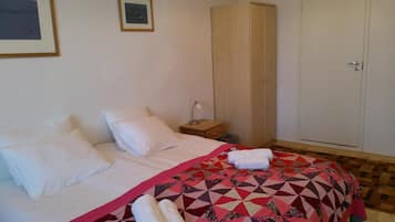 Quarto com cama, almofadas, colcha, guarda-roupa de madeira, mesa de cabeceira e uma porta.