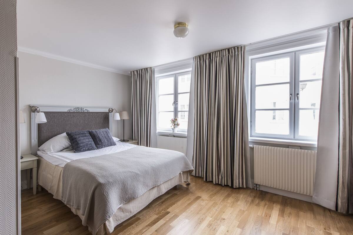 A bedroom with a bed, nightstands, a window with curtains, and a radiator.