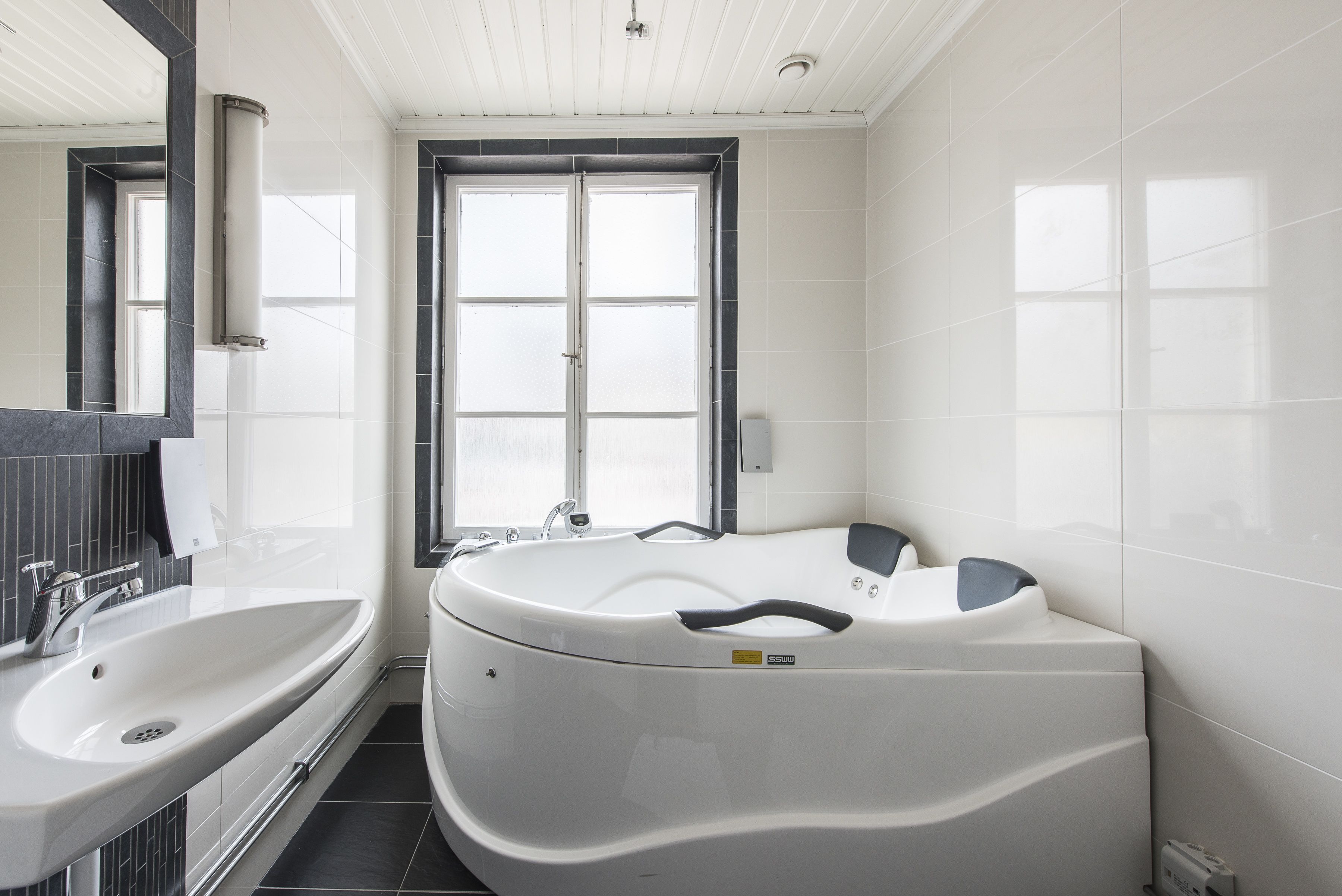A modern bathroom with a large bathtub, a sink, and a mirror.
