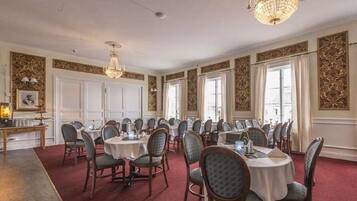 A formal dining room with round tables and chairs, chandeliers, and decorative wall panels.