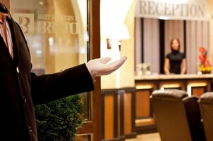 Una persona con abrigo negro extiende la mano hacia un mostrador de recepción con el rótulo "RECEPTION".