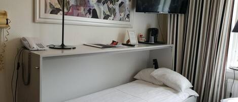 Habitación de hotel con cama, escritorio con lámpara, teléfono, televisión y un cuadro en la pared.