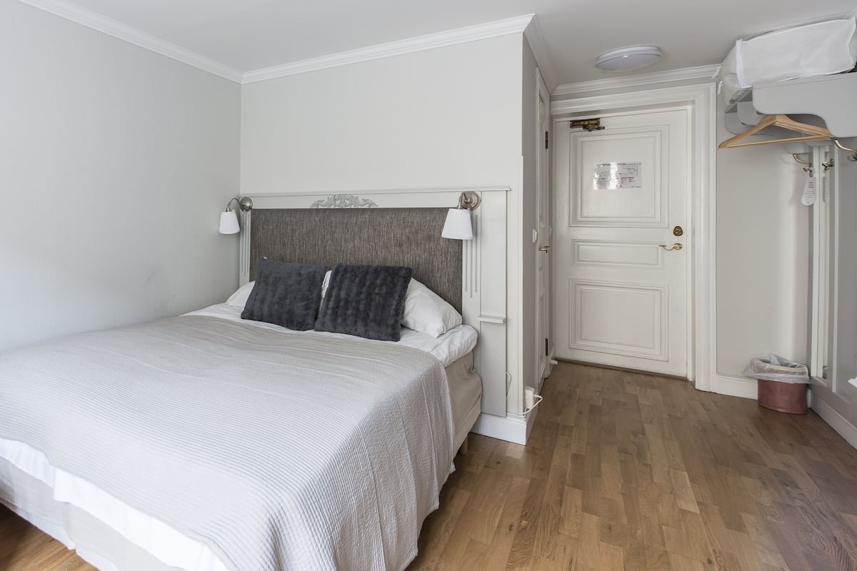 A neatly arranged bedroom with a bed, bedside lamps, a wardrobe, and a door with a sign.