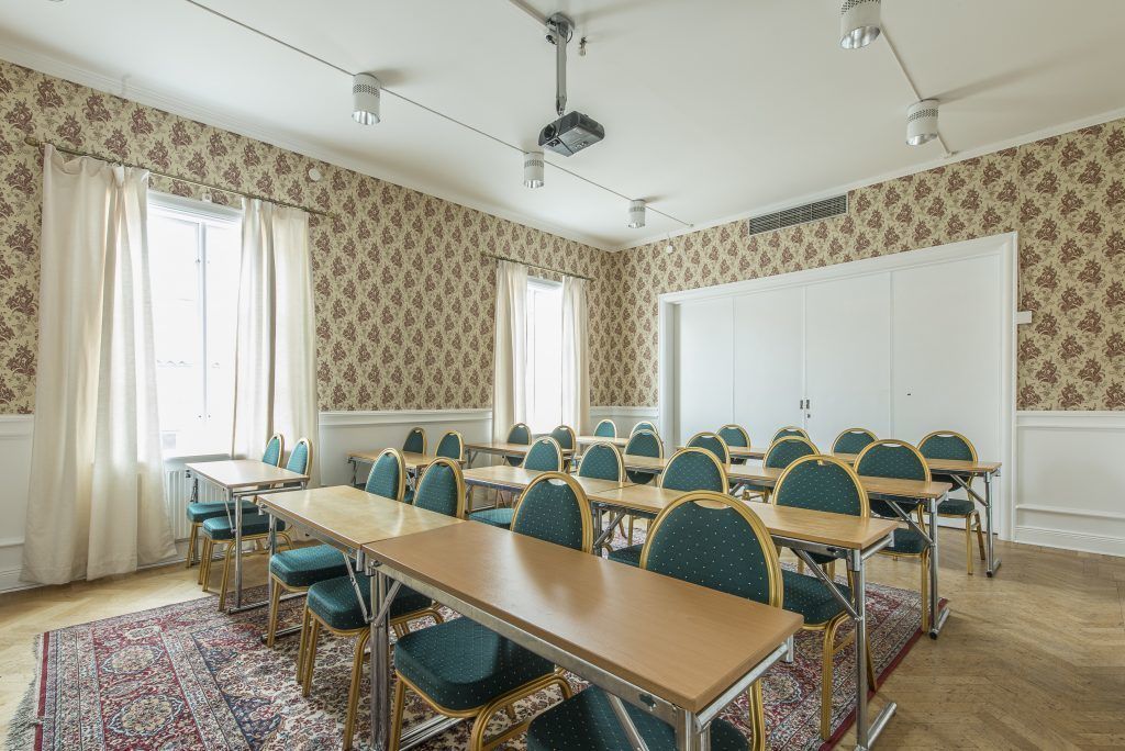 Un salón de conferencias con una mesa larga, varias sillas, un proyector y una pizarra.