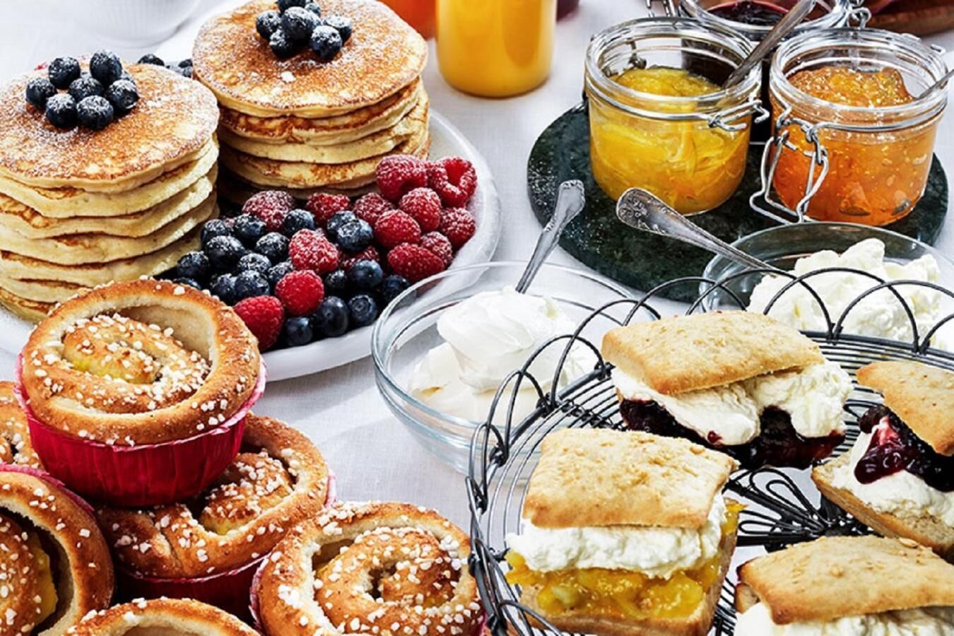 A breakfast buffet with pancakes, berries, pastries, and jams.