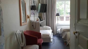 A hotel room with a bed, bedside table, chair, TV, and a window with curtains.