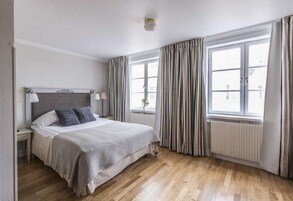 Un dormitorio con cama, mesitas de noche, ventana con cortinas y un radiador.