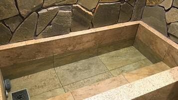Una bañera con revestimiento de piedra, suelo de baldosas y desagüe.