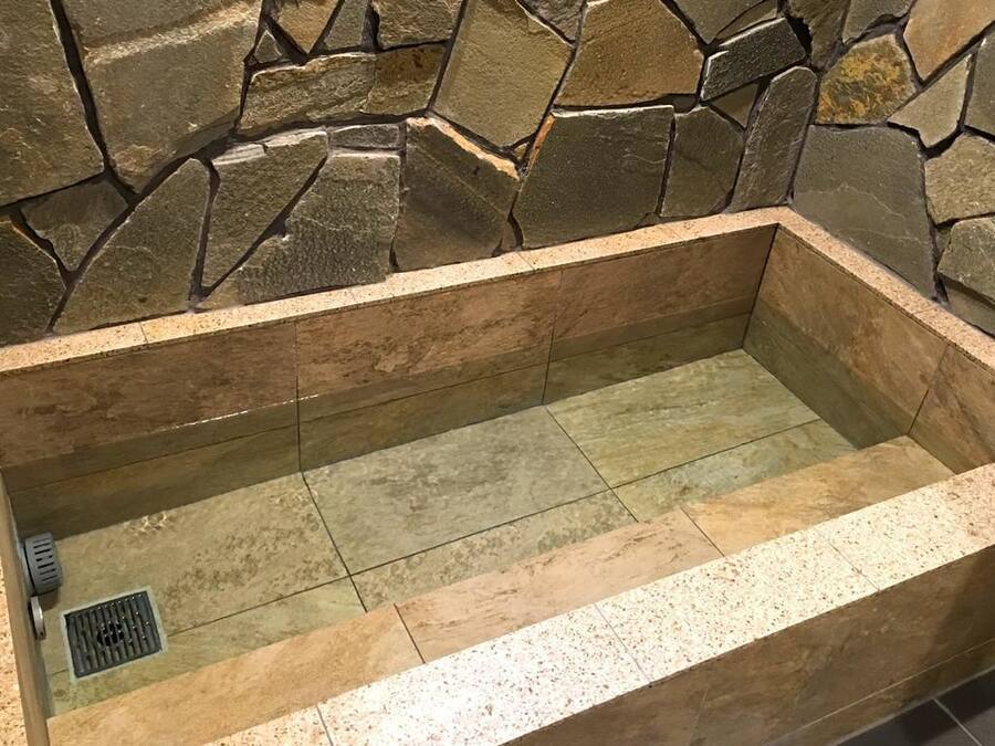 Una bañera con revestimiento de piedra, suelo de baldosas y desagüe.