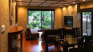 A modern living room with a sofa, chairs, a TV, and a view of greenery outside. - Hananobou Kinkakuji-michi (Kyoto)