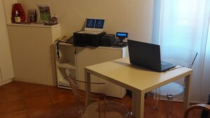 A small office with a desk, laptop, printer, and a clear plastic chair. - B&B San Francesco (Siena)