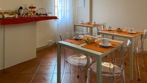 A dining area with clear chairs, tables set with white plates, orange placemats, and clear glassware. - B&B San Francesco (Siena)