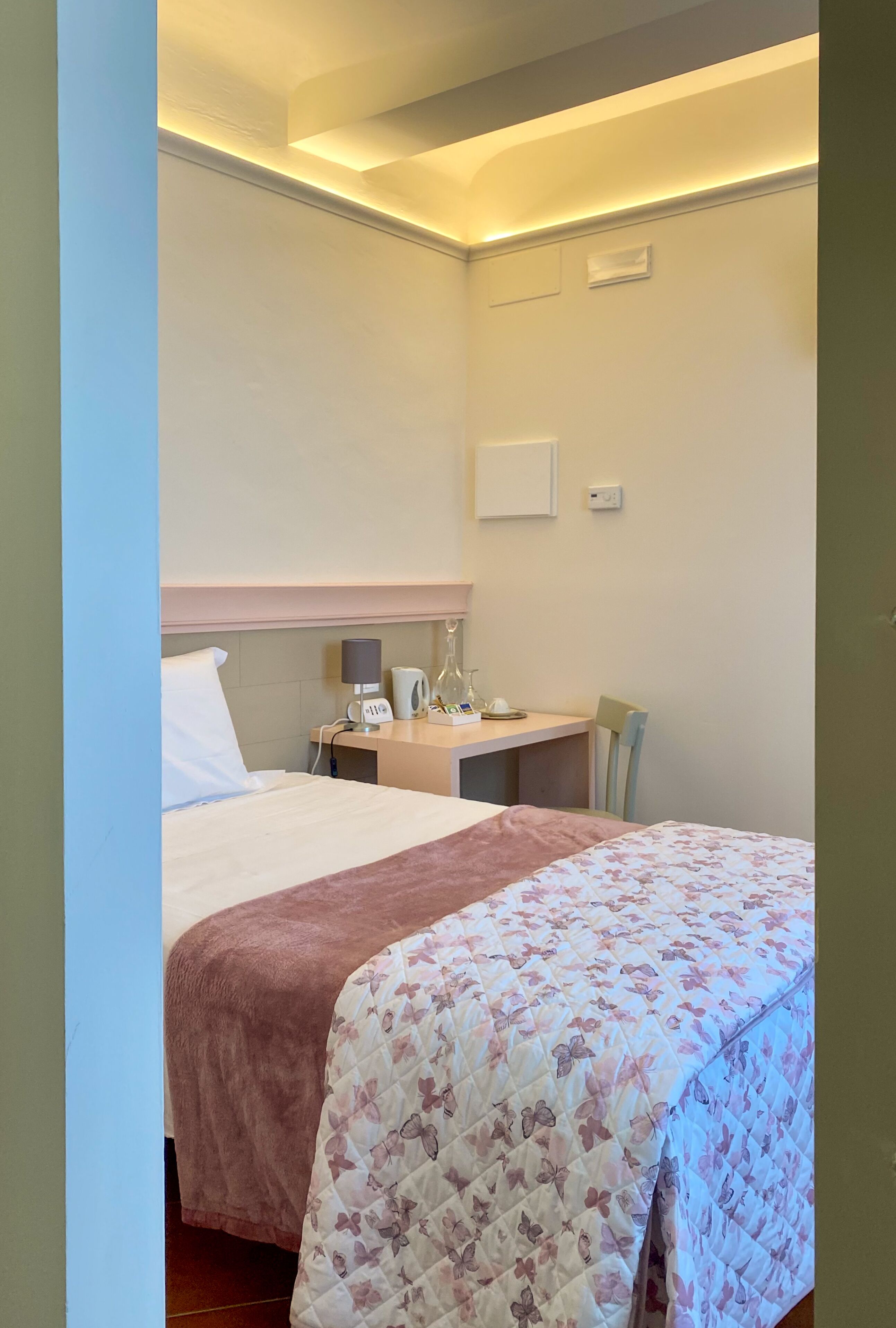 Habitació d'hotel amb llit, escriptori amb làmpada, cadira i taula petita amb batedora i tasses.