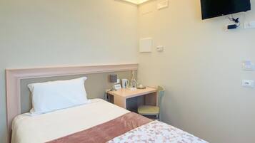 A hotel room with a bed, a desk, a chair, a TV mounted on the wall, and a window.