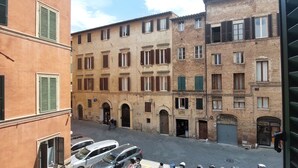 A narrow street with parked cars and a building with multiple windows and doors. - B&B San Francesco (Siena)