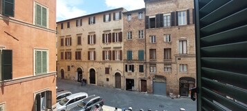 Una stretta via con auto parcheggiate e un edificio con numerose finestre e porte.