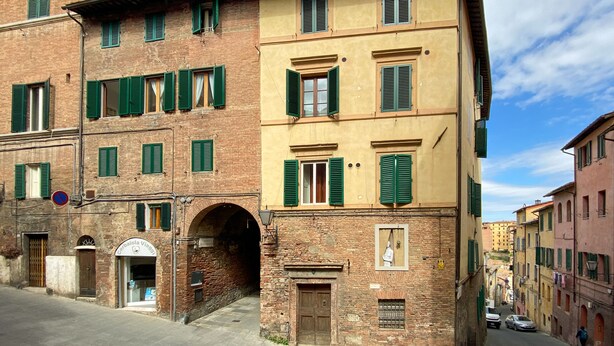 A historic building with multiple stories, green shutters, and a visible entrance. - B&B San Francesco (Siena)