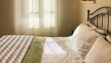A neatly made bed with a quilt and a green throw blanket, a metal headboard, and a shelf with books and a box.