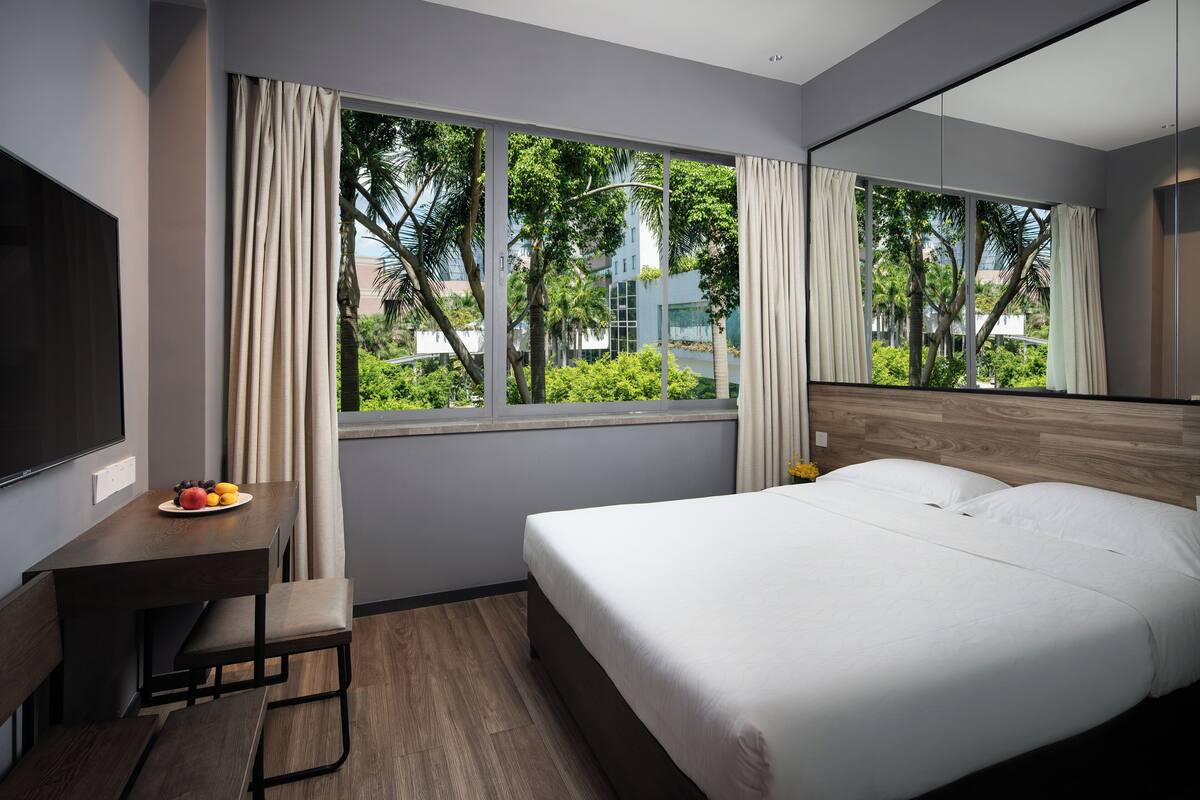 A modern hotel room with a bed, a desk with a chair, a TV, and a window with curtains.