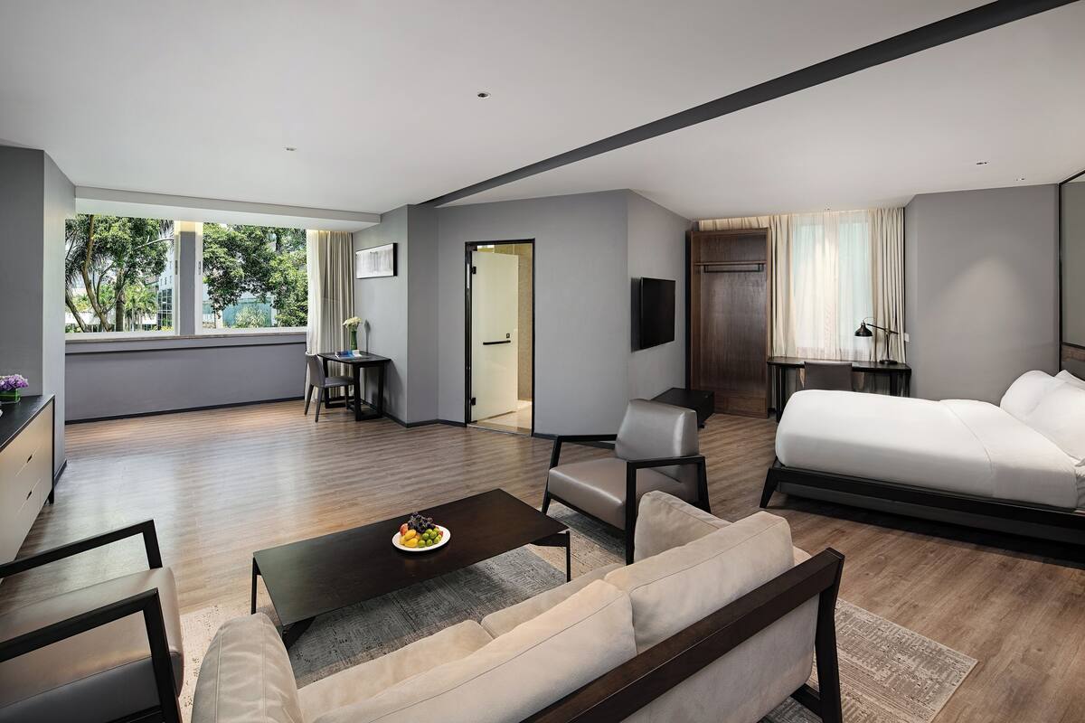 A modern hotel room with a large bed, a sofa, a coffee table, and a desk area.