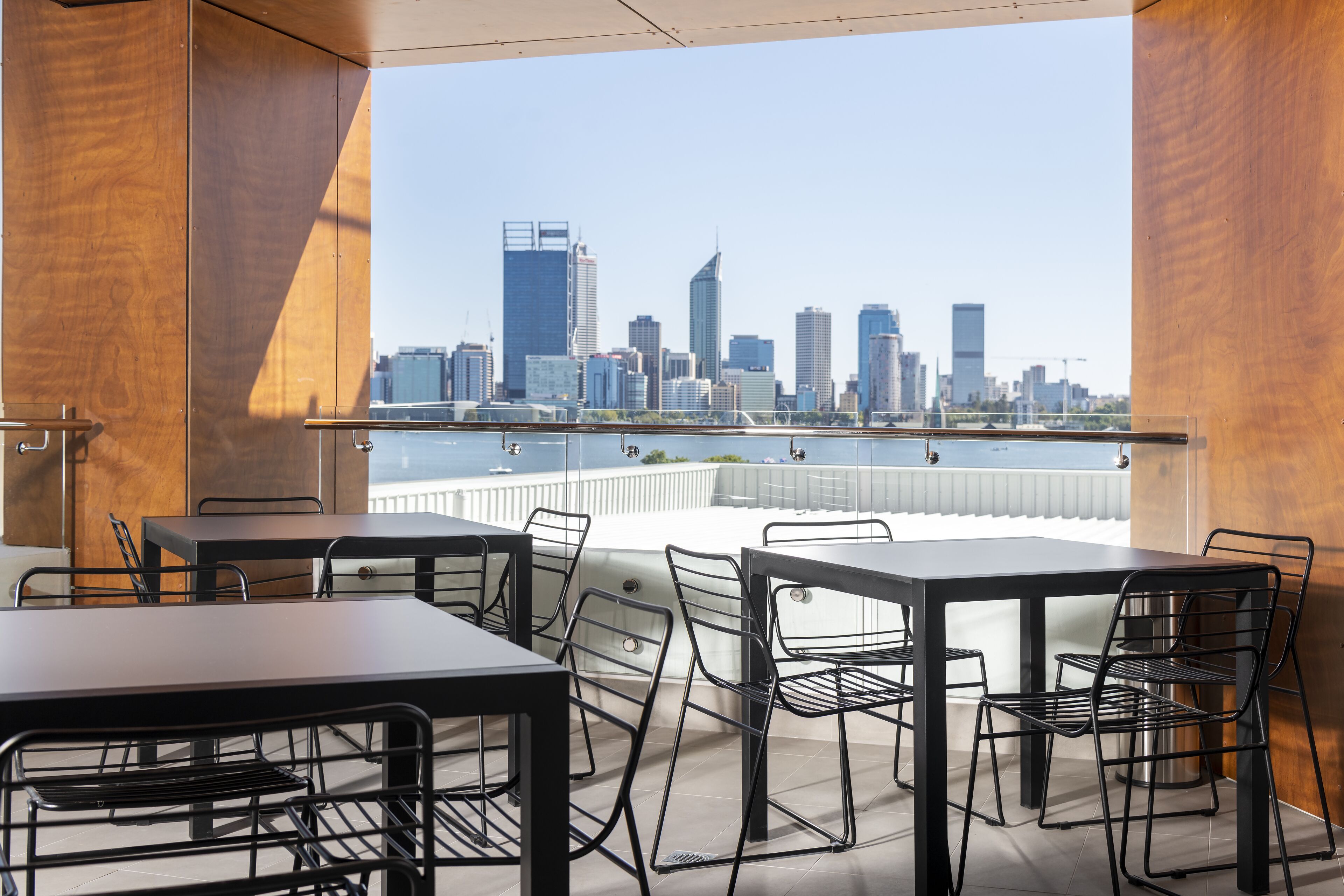 Un comedor moderno con mesas y sillas, vistas a un horizonte urbano y un balcón con barandilla.