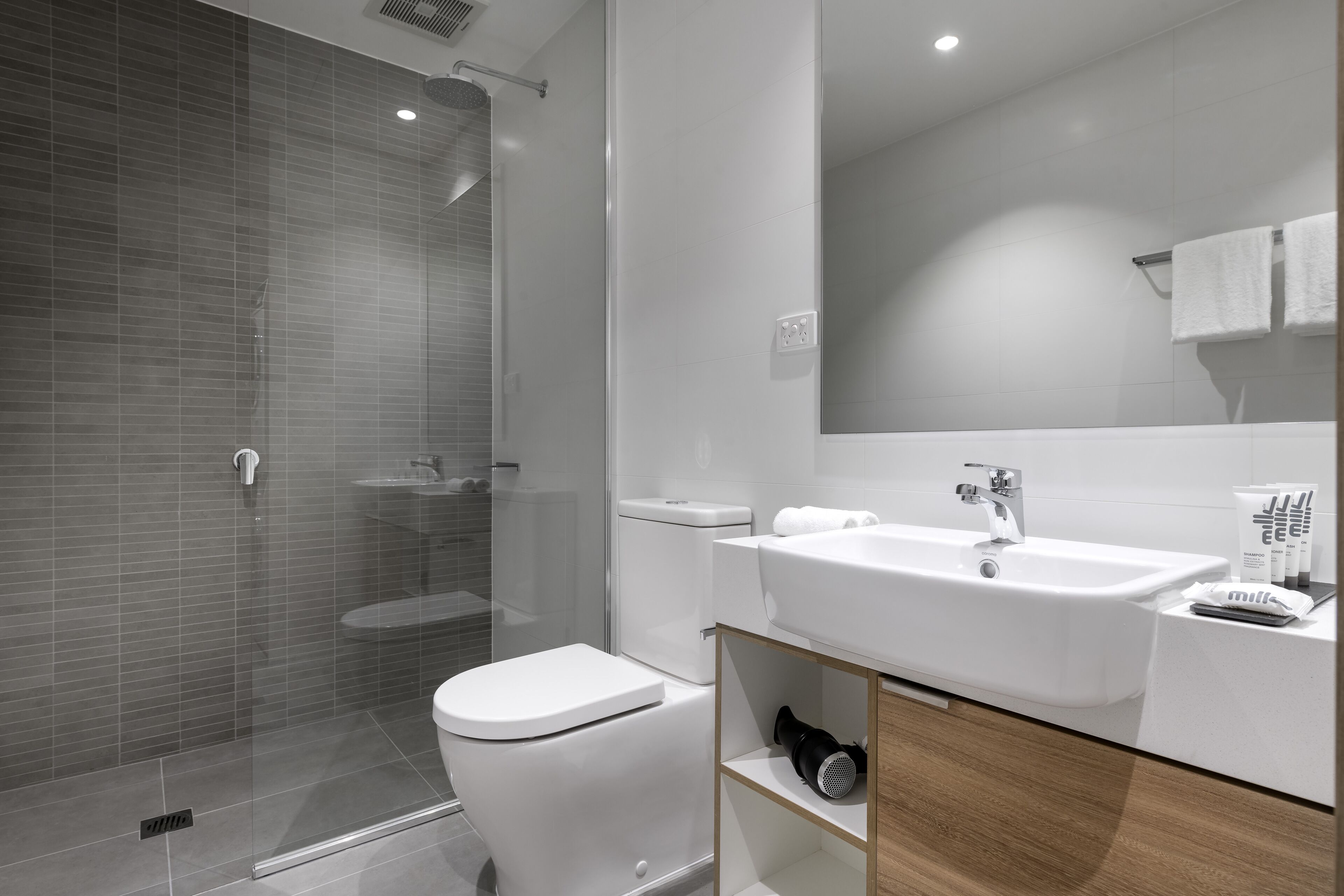 A modern bathroom with a glass-enclosed shower, a white toilet, and a sink with a mirror above it.