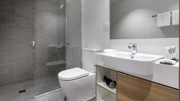 A modern bathroom with a glass-enclosed shower, a white toilet, and a sink with a mirror above it.