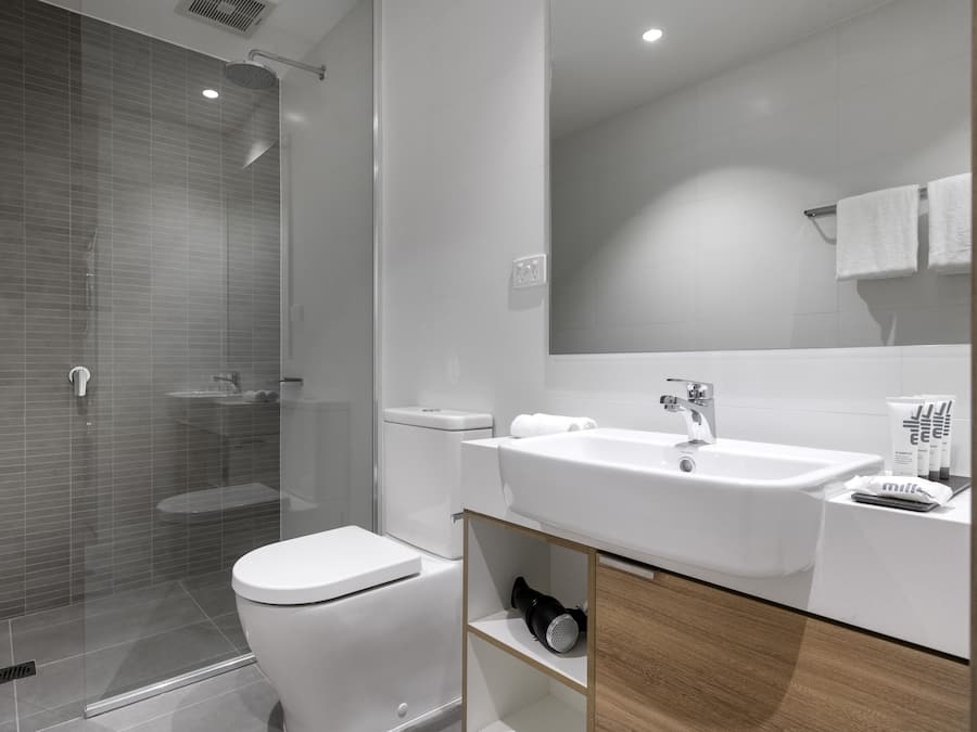 A modern bathroom with a glass-enclosed shower, a white toilet, and a sink with a mirror above it.